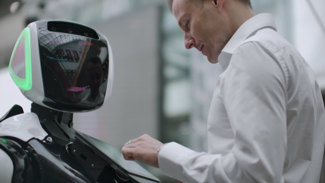 человек стоит с роботом-ботом и задает ему вопросы и просит помощи, нажав на экран на теле робота. взаимодействие человека и робота в современном мире