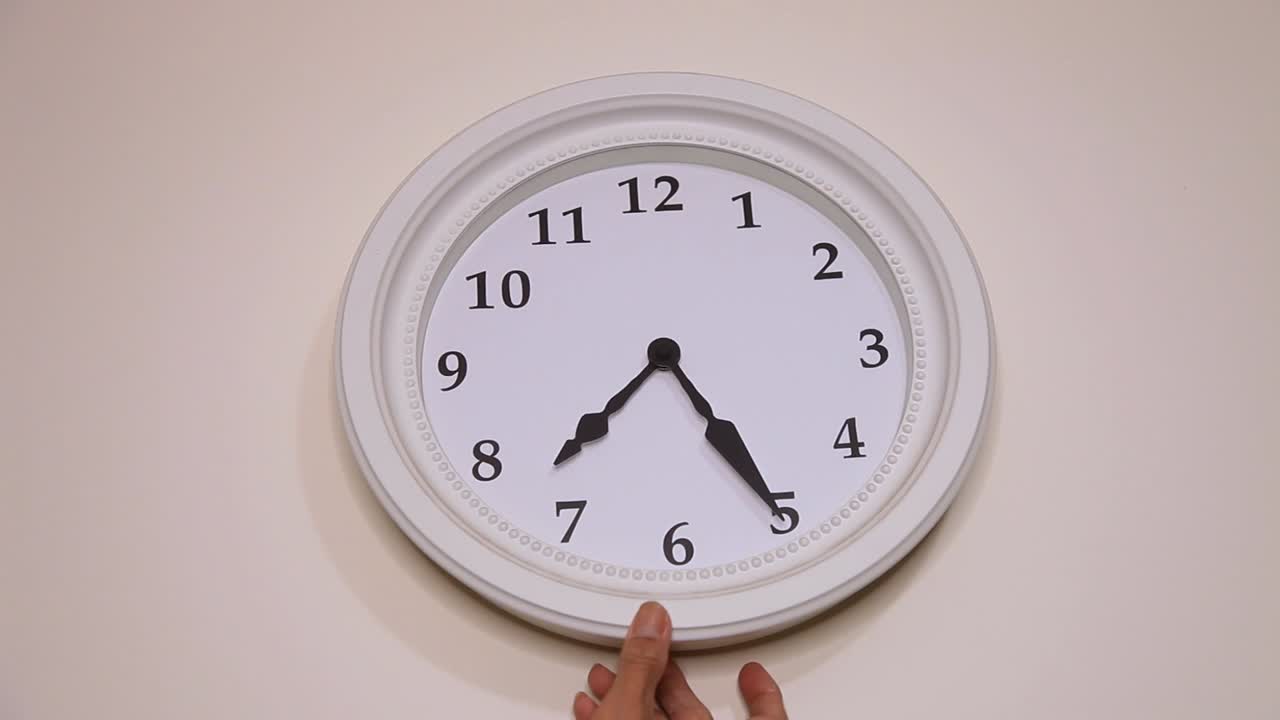 Hand adjusting or repositioning a clock on the wall, close up