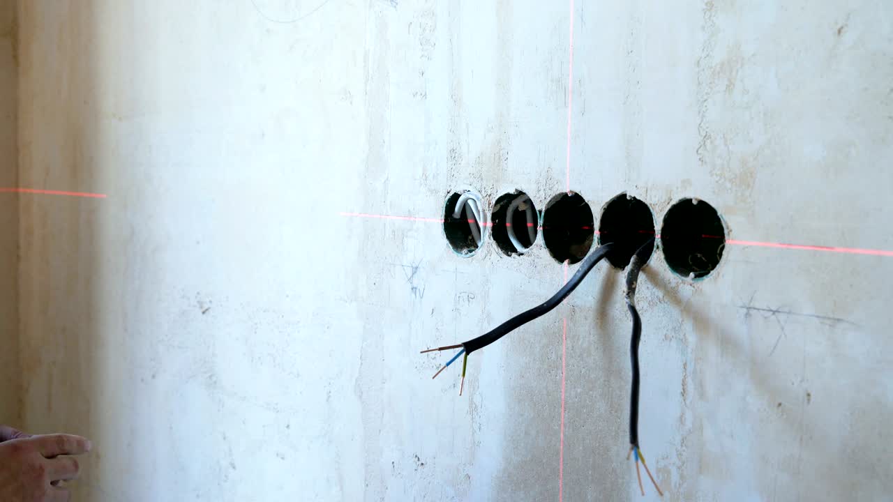 electricista comprobando los parámetros técnicos con cinta métrica y herramienta láser de haz rojo en el sitio de construcción