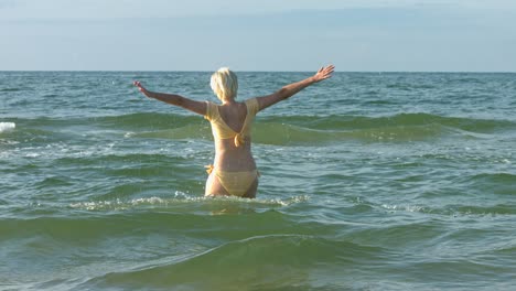 a woman wearing a pastel yellow bikini jumping up through a wave in the ocean water