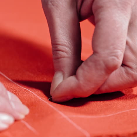 female hands of the skilled worker putting the pin to the fabric. red cloth with white lines and a tailor pinning the material on the table. concept sewing and handicraft.