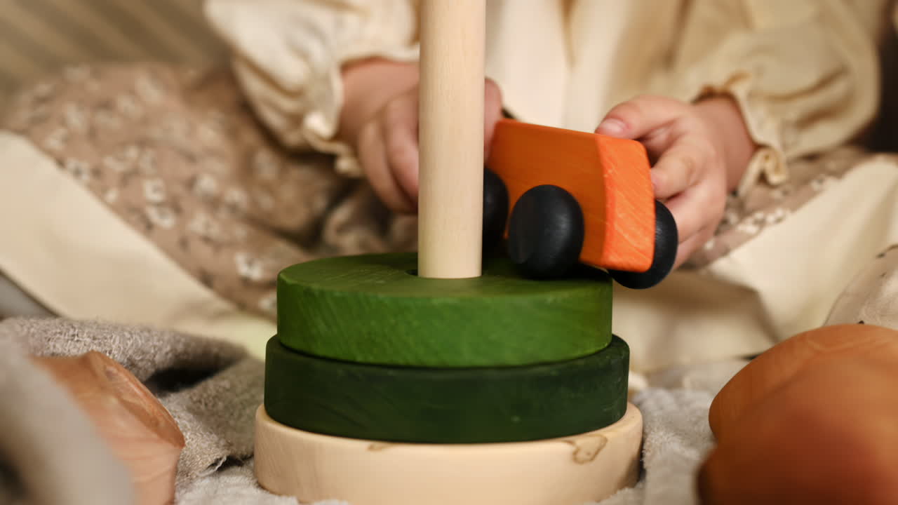 Little girl's hand playing with a a wooden rolling bus toy on the wooden pyramid. Ecological and sustainability concept