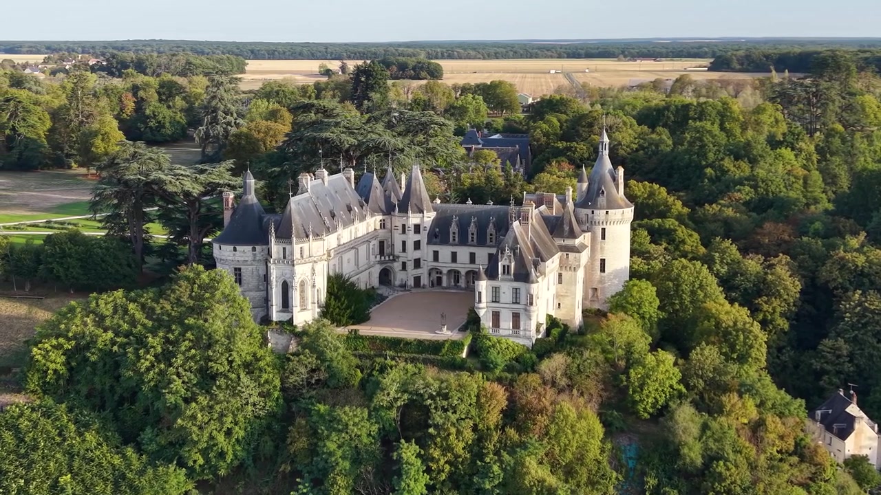 Lento volo orbitale cinematografico di un drone attorno allo Château de Chaumont-sur-Loire, che rivela le sue torri, il cortile, i terreni boscosi e l'ampio paesaggio agricolo