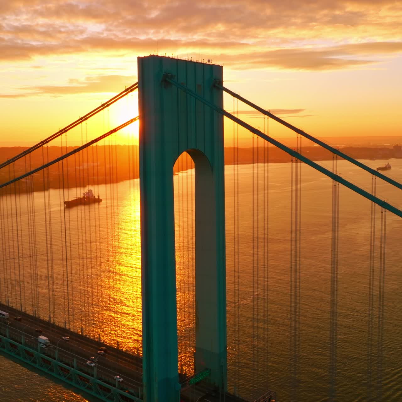 Whitestone bridge in the rays of setting sun. Cars going along the bridge back and forth. Yachts and boats sailing along the East River
