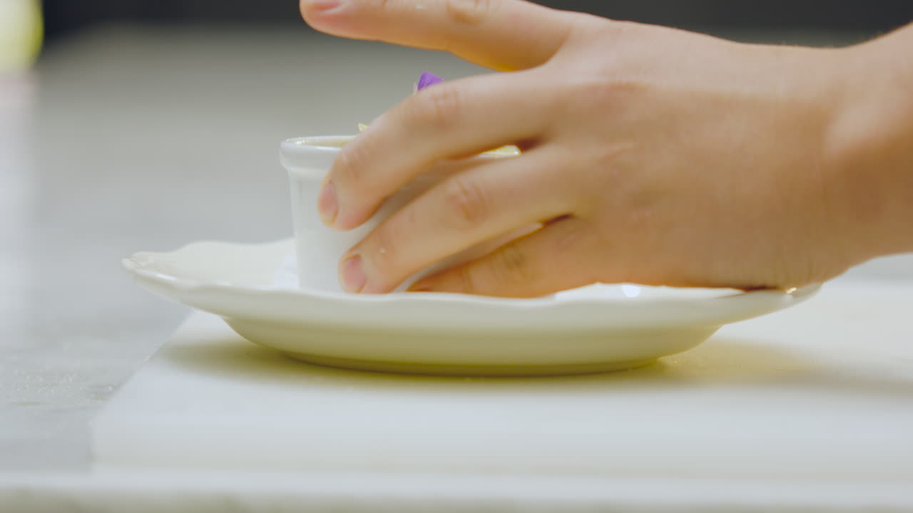 Close-up of a chef placing a creme brulee decorated with flowers and blueberries on a white plate