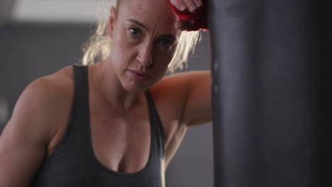 portrait of caucasian female boxer leaning on punching bag at the gym