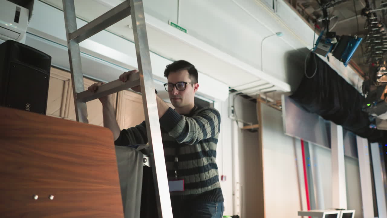 studio worker climbing ladder adjusting lighting SL-200W, preparing for broadcast production, adjusting equipment for proper lighting in a professional studio environment, production setup
