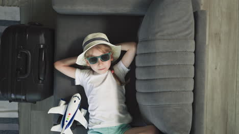 relaxed preschooler adjusts stylish sunglasses lying on sofa