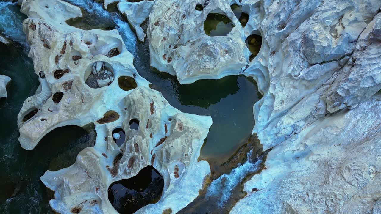 A moving shot highlights detailed rock formations by the river, showing people wading and enjoying the water at Tinipak River, Philippines