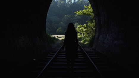 a young woman walks through a tunnel towards daylight on the railway tracks