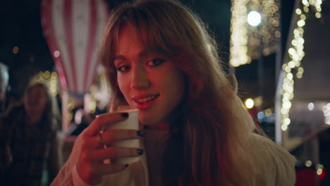 smiling girl drinking coffee at night fair closeup. woman sipping beverage