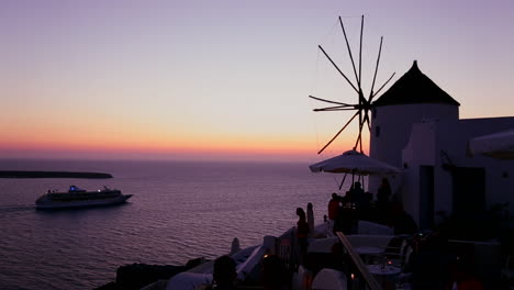 a cruise ship passes windmills at dusk or sunset on the romantic greek island of santorini at dusk