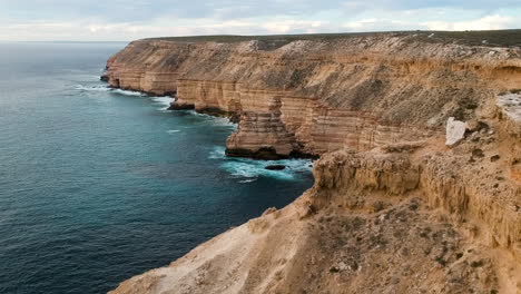 Video-Cinematográfico-De-Drones-Desde-Un-Acantilado-En-El-Desierto-Interior-Durante-La-Hora-Dorada-Del-Atardecer-Con-Grandes-Olas-Azules-Y-árboles-Verdes