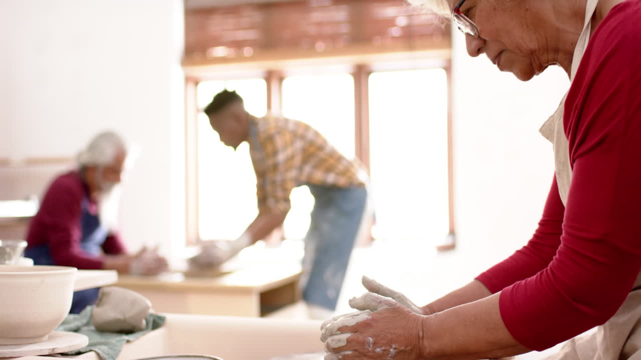 Focused biracial male and female potters using potter's wheel in pottery studio, slow motion