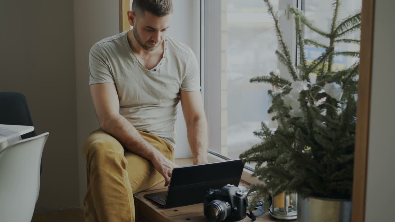 Man Working on Laptop by Window with Christmas Tree