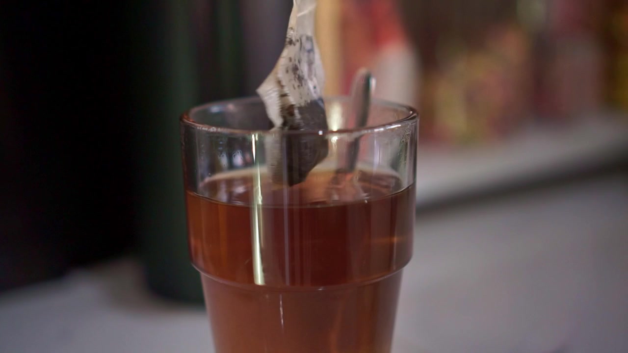 Bustina di tè in infusione in un bicchiere trasparente pieno di acqua calda, preparazione della bevanda in primo piano, processo di infusione, concetto di preparazione del tè fatto in casa.