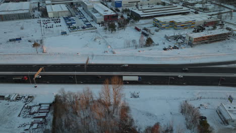 Eine-Draufsicht-Auf-Eine-Hauptstraße-Im-Schneebedeckten-Stadtteil-Dąbrowa-In-Gdynia,-Die-Fahrzeuge-Zeigt,-Die-Sich-Inmitten-Einer-Winterlichen-Umgebung-Bewegen,-Gesäumt-Von-Industrieanlagen-Und-Kahlen-Bäumen