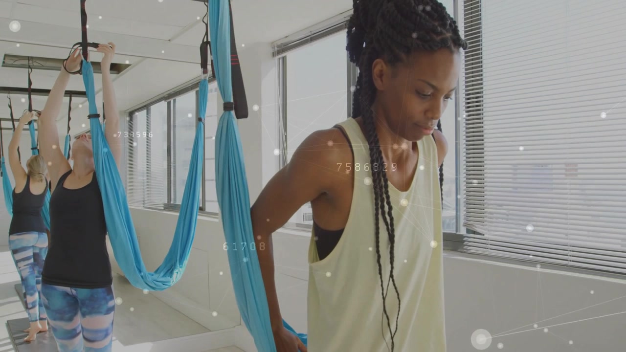 Lezione di yoga che inizia con donne che fanno scivolare la vita di seta, si allungano sopra la testa, regolano le maniglie blu e preparano le pose
