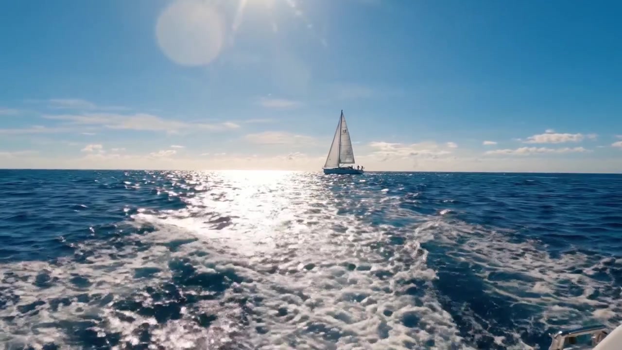 A tranquil sailing experience on the shimmering ocean, with sunlight glistening on the water as a lone sailboat gracefully navigates through the waves.