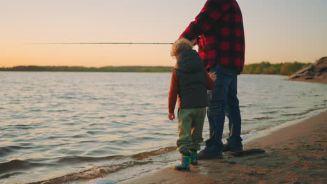 calm family rest on river shore father and little son are fishing beautiful sunset in autumn or spring evening