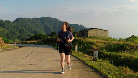 Frontalansicht-Einer-Asiatischen-Frau,-Die-Bei-Sonnenuntergang-Einen-Wanderrucksack-über-Den-Landweg-Trägt