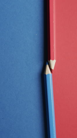 vertical video of overhead view of red and blue crayon on blue and red background, in slow motion