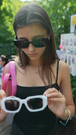 young woman shopping for sunglasses at a market