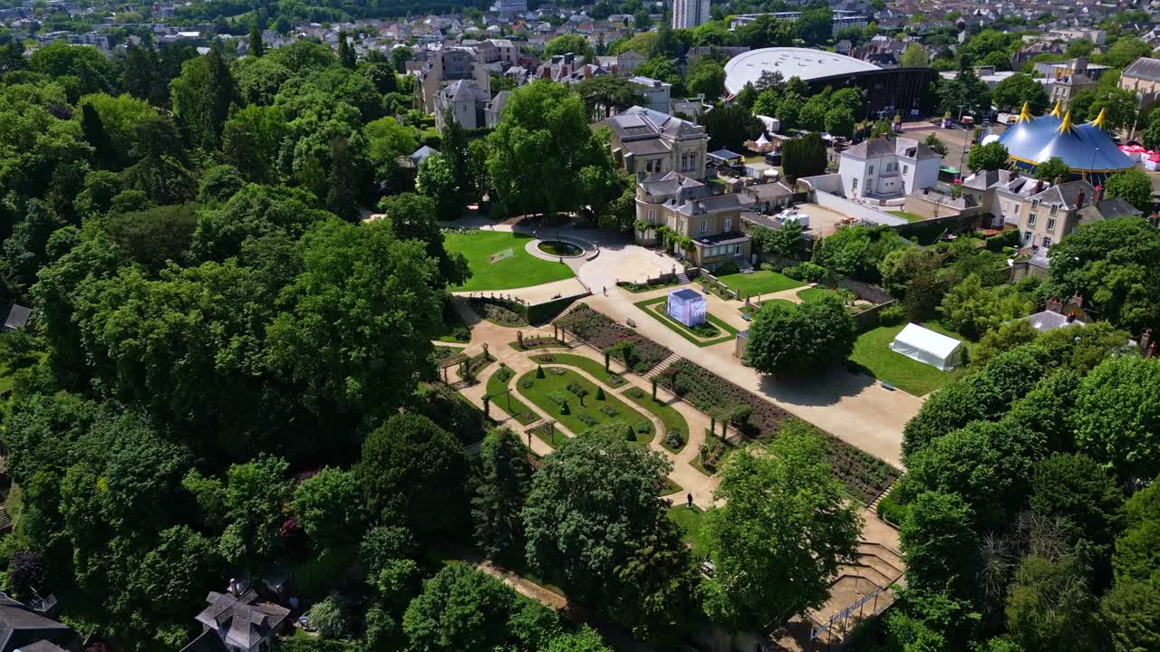 Top-down drone view of Jardin de la Perrine in Laval, with rose garden, circus tent, trees, and distant cityscape - France
