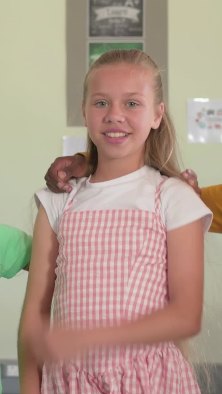 Vertical video: Bending boy in yellow top rising draping arm on girl pink dress posing school