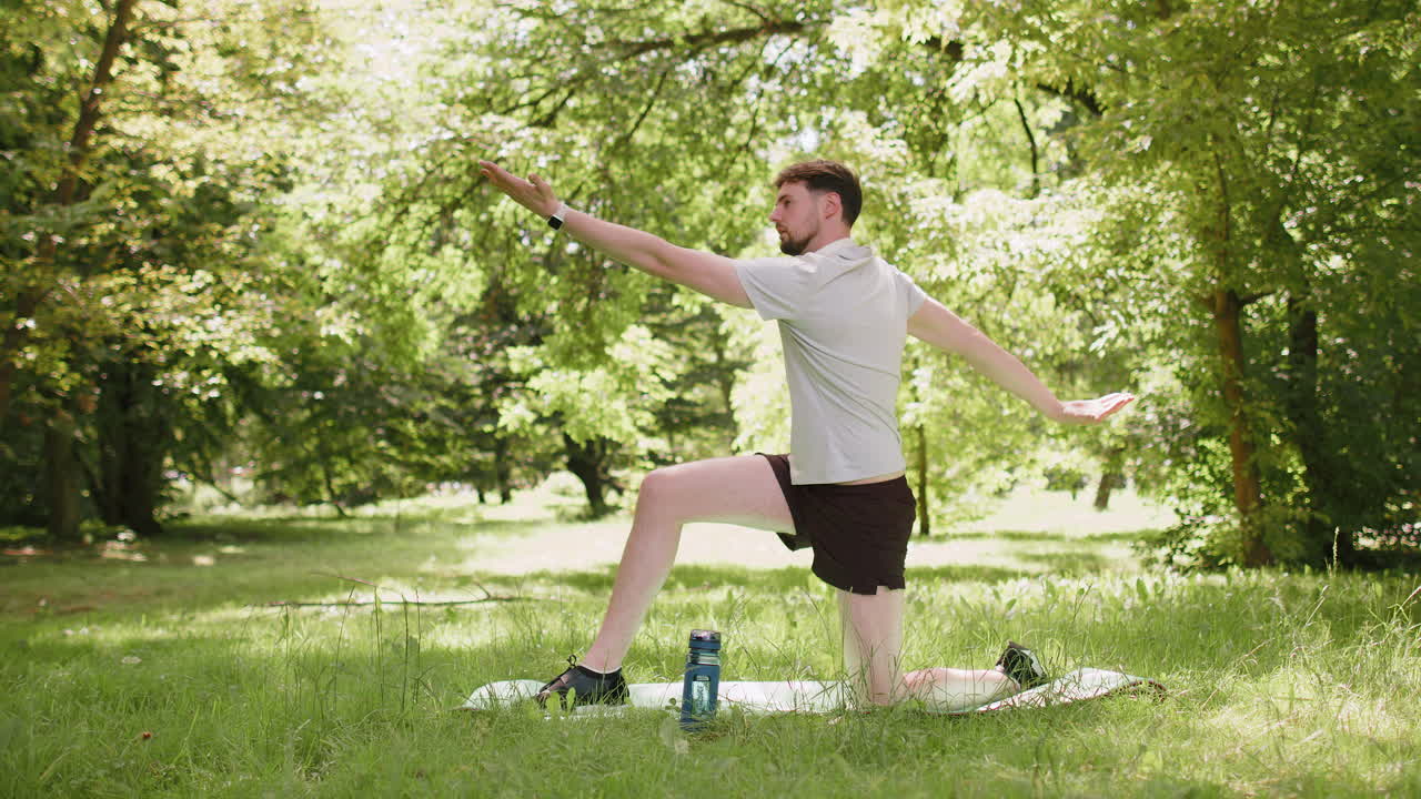 Sporty fit young man doing workout yoga warrior pose in park on a sports mat arms outstretched