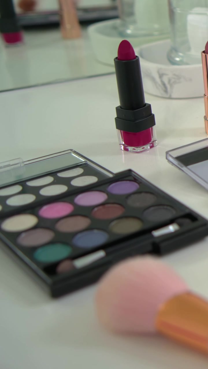 Vertical video: Panning camera over vanity, revealing bright pink lipstick, showcasing palettes
