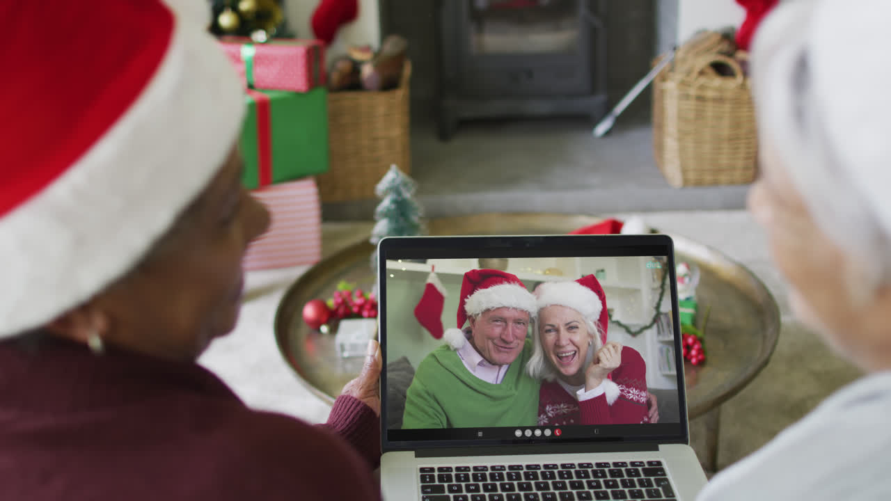 diversas amigas mayores que usan una computadora portátil para una videollamada de navidad con una pareja feliz en la pantalla