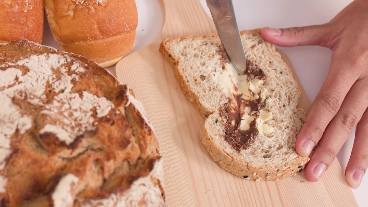 Close-up of hands spreading chocolate and peanut butter on bread with a metal knife.