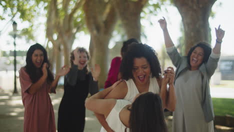 lesbian brides dancing and kissing in a park after wedding ceremony while bridesmaids applauding