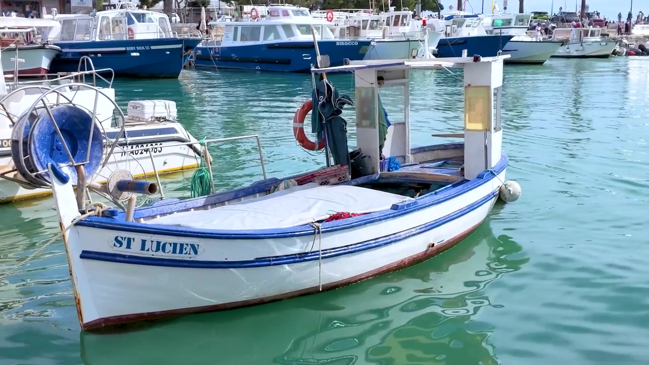Tradizionale barca da pesca in legno riposa su acque calme e turchesi in un soleggiato porto mediterraneo.