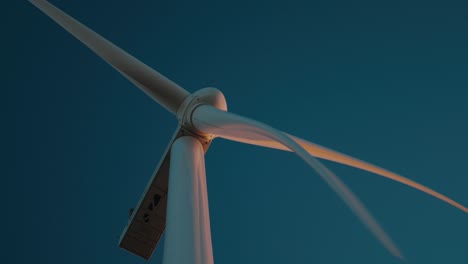 a wind turbine slowly spinning against a deep blue sky at dusk, close-up view