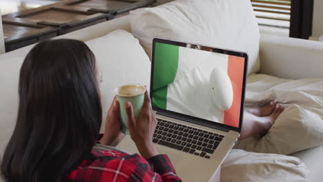 mujer biracial viendo una computadora portátil con una pelota de rugby con la bandera de la costa de marfil en la pantalla