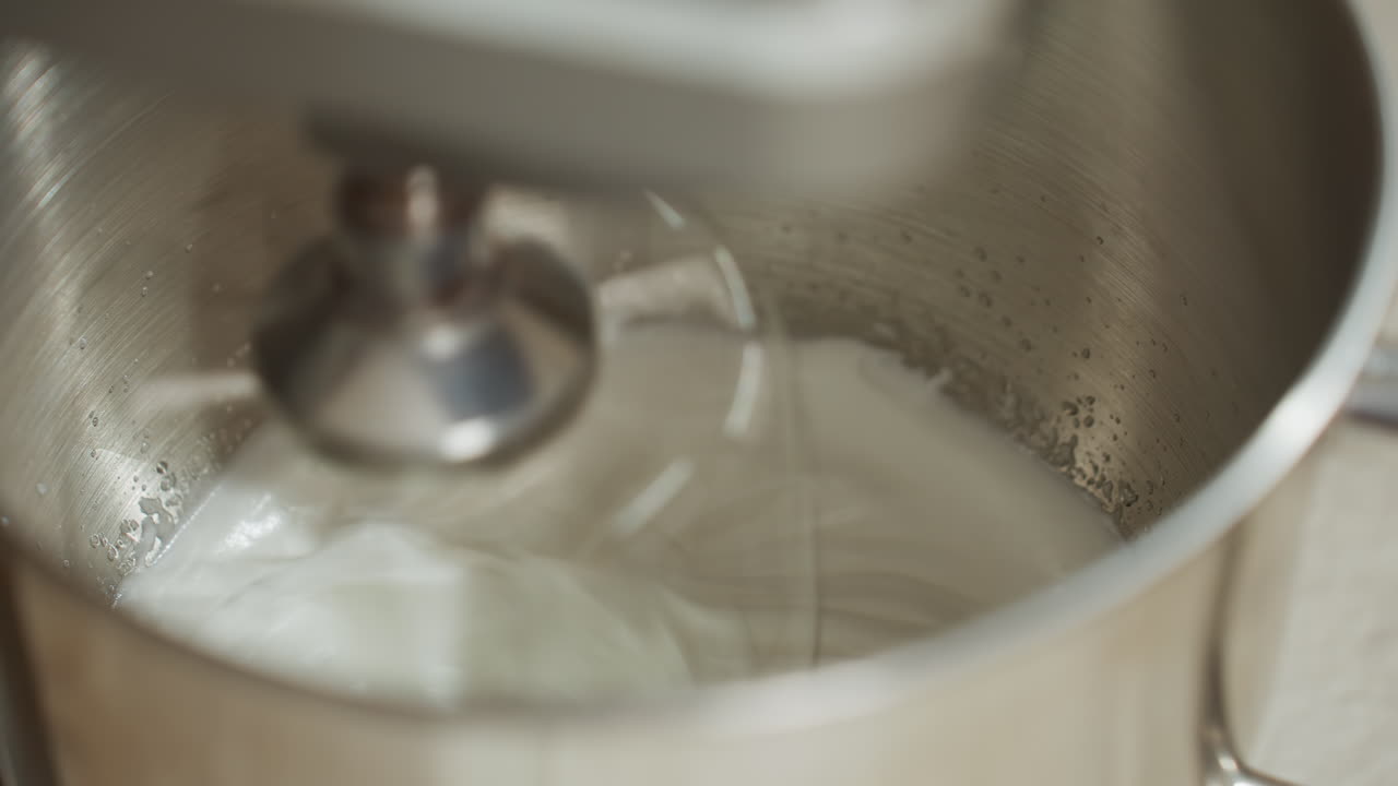 Close up of electric mixer whipping mashed ingredient inside stainless steel bowl, with visible swirl motion and smooth creamy texture forming during active mixing process