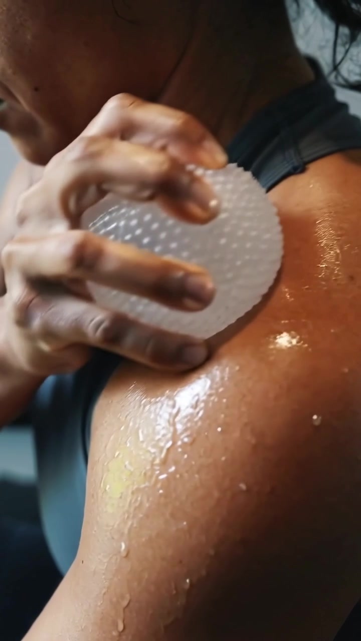 Video verticale: Donna in forma che preme e strofina un cuscinetto in silicone sul deltoide oliato in palestra per la pelle.