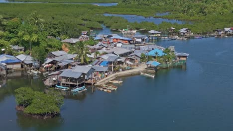 an aerial drone shot of day-asan floating village in surigao del norte - philippines, showing wooden walkways and buildings on stilts with metal roofs and lush landscape