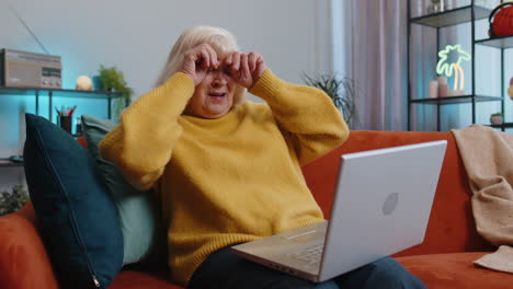 grandmother old woman use laptop surprised by bad news fortune loss fail lottery results at home