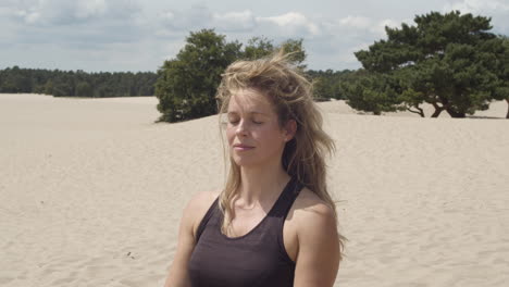 Close-up-of-woman-sitting-with-closed-eyes-in-sand-dunes