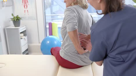 caucasian female physiotherapist massaging lower back of female senior patient at rehab center