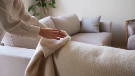 person arranging a cozy knitted blanket on a sofa in a living room