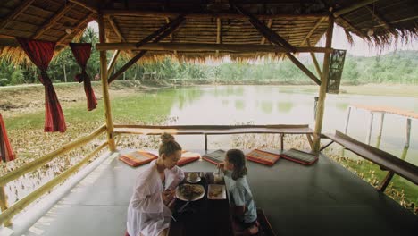 the happy family eat and drink tasty beverages spending time in local floating cafe on water. mother and daughter having breakfast outdoors