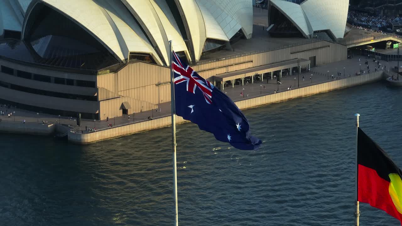 SYDNEY, AUSTRALIA - APRIL 1, 2024: The Australian and the Aboriginal flag waving in the wind at the Darling Harbour and Cockle Bay. Aerial drone shot. In the background: the Sydney Opera House.