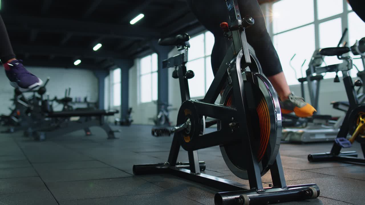 Closeup legs of group unrecognizable friends at gym exercising on stationary bike at class in gym