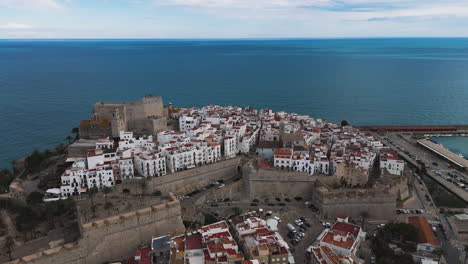 aerial establishing of peniscola castle and marina edge as waves crash along rock lined shore