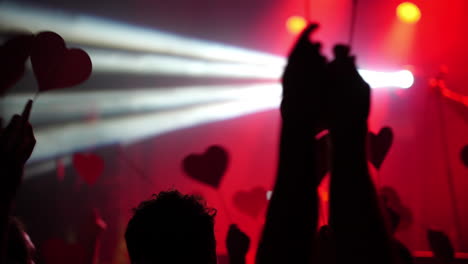 crowd of hands holding heart shapes illuminated by vibrant stage lights in a lively atmosphere