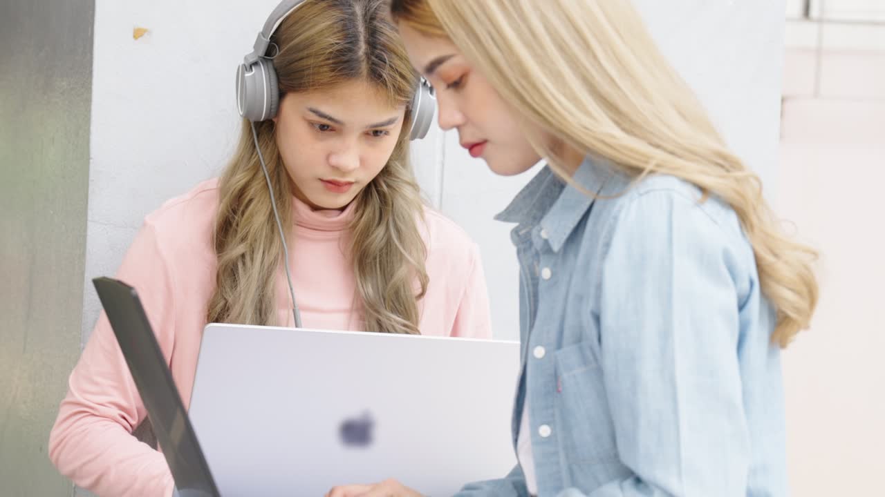 Two Asian girls student partners are working on a laptop help study together